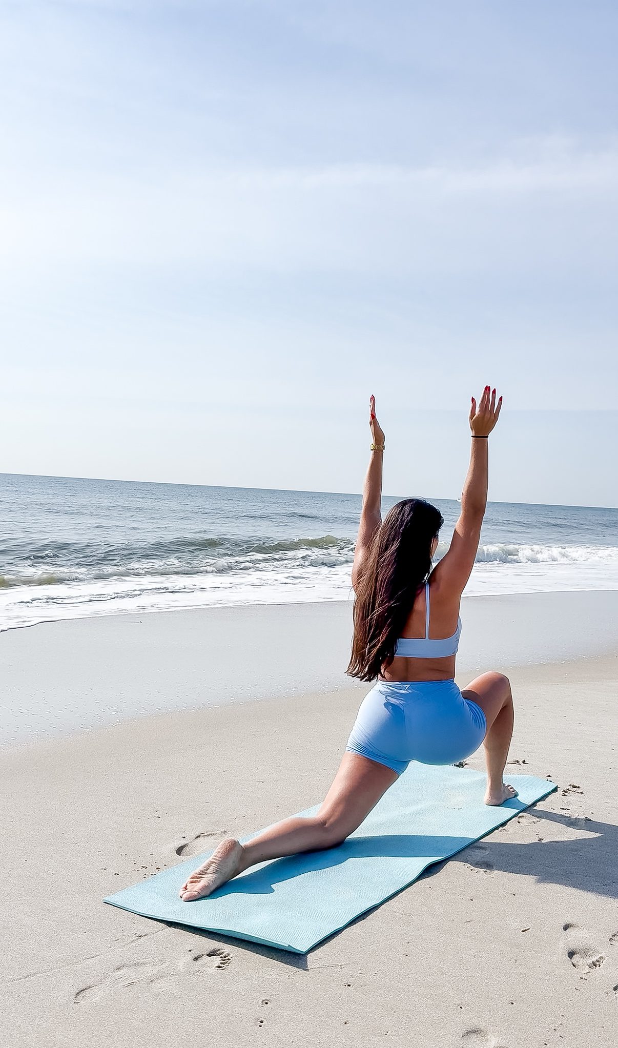 Woman standing on the beach in a lunge pose with arms raised