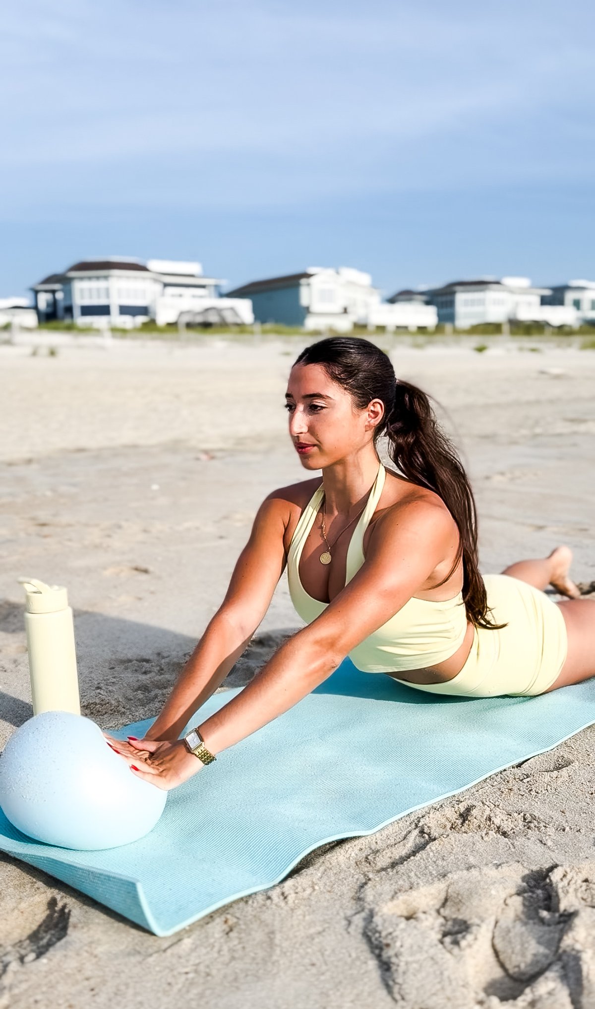 Amanda stretching forward with a Pilates ball on the beach