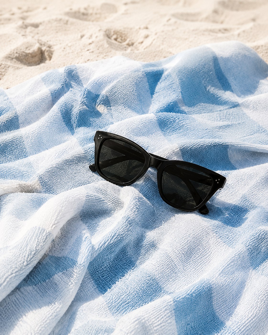 Sunglasses resting on a blue gingham beach towel