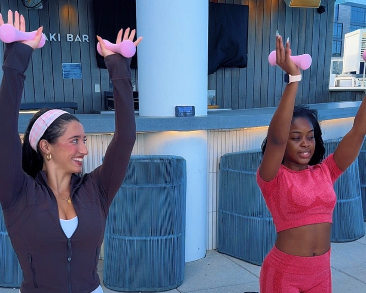 Amanda coaching a client through an overhead arm exercise with pink hand weights at Wave Resort